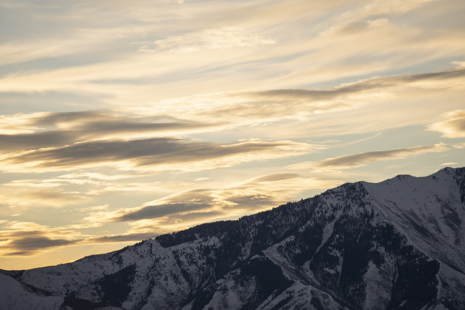 Clouds lit yellow as the sun sets over snowy mountains